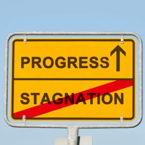 Road sign saying progress with an arrow ahead and the word stagnation crossed out